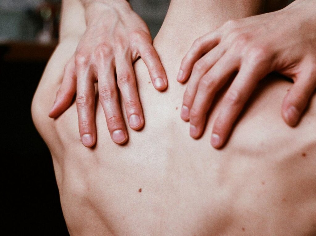 Dłonie fizjoterapeuty na odcinku lędźwiowym pleców pacjenta podczas terapii
